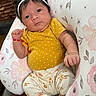 Gia is registered to the contest to win money with this photo: baby, infant, child, headband, flower, yellow_shirt, polka_dot, floral_pants, bracelet, cushion, pattern, pink_flowers, white_socks, hand, face, eyes, hair, indoor, person, portrait