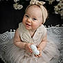 baby, child, smile, headband, blue_eyes, dress, tulle_skirt, flower, white_flower, lace_blanket, sitting, portrait, cute, indoor, infant, holding_object, soft_lighting, closeup, happy, adorable