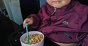 Leyah participe au concours pour gagner de l'argent avec cette photo : toddler, child, blue_eyes, cereal, bowl, spoon, high_chair, maroon_jacket, indoor, furniture, table, face, person, young_child, meal, snack, expression, hair, seated, cute