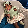Ari is registered to the contest to win money with this photo: baby, infant, pacifier, headband, bow, clothing, dress, floral, lace, socks, person, indoor, cushion, blanket, blue, beige, cute, portrait, child, relaxed