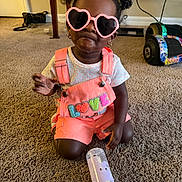 Kreari is registered to the contest to win money with this photo: toddler, child, sunglasses, heart_shaped, pink_overalls, love_text, baby_bottle, carpet, indoor, cute, fashion, accessories, hair_buns, earrings, playful, smiling, person, casual, home, toy_car