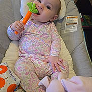 Emilia joined the competition — help win amazing prizes! baby, child, infant, smiling, sitting, portrait, face, eyes, teether, toy, carrot, floral_pajamas, onesie, highchair, cushion, blanket, stuffed_animal, bunny, indoors, happy
