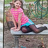 Rosaleen is registered to the contest to win money with this photo: bench, blue_shorts, casual_clothing, child, daylight, figurines, garden, girl, grass, hose, leaves, nature, outdoor, pink_shirt, plants, playful, pottery, smiling, stone_bench, tree