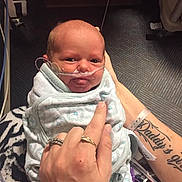 Rosaleen joined the competition — help win amazing prizes! baby, infant, blanket, nasal_tube, hand, rings, tattoo, hospital, medical_equipment, floor, person, swaddled, newborn, care, healthcare, indoor, closeup, holding, parent, comfort