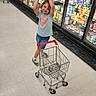 aisle, casual_clothing, child, floor, food, grocery_items, grocery_store, happy, indoor, person, playful, pose, refrigerator, shoes, shopping_cart, shorts, smile, socks, supermarket, young_child