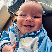 Tao participe au concours pour gagner de l'argent avec cette photo : baby, blue_jacket, child, closeup, clothing, cozy, cute, expression, face, hand, happy, indoor, infant, nike_logo, person, portrait, sitting, smile, warm_light, young_child