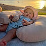 baby, infant, beach, sunset, pillow, hat, toy, smile, chubby, ocean, sand, water, blanket, portrait, outdoors, golden_hour, relaxation, cute, sunlit, family