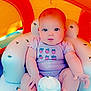 Octavia is registered to the contest to win money with this photo: baby, infant, child, inflatable_chair, pool_toy, summer, cute, pink_clothing, strawberry_print, indoors, sitting, barefoot, chubby, bright_colors, orange, blue, playful, water_drops, expressionless, adorable