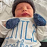 baby, newborn, sleeping, hat, mittens, clothing, white_blanket, blue_pants, sweater, text_on_clothing, indoor, cozy, peaceful, portrait, infant, child, person, cute, resting, soft