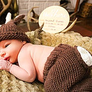 Neyland is registered to the contest to win money with this photo: baby, newborn, knit_hat, knit_pants, antlers, wooden_sign, blanket, indoor, cute, infant, resting, soft_texture, warm_colors, portrait, child, sleepy, cozy, decor, closeup, adorable