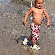Matteo is registered to the contest to win money with this photo: child, toddler, water, splash_pad, summer, bare_chest, shorts, crocs, water_droplets, outdoor, play, fun, sunny, daytime, concrete, grass, happy, walking, boy, casual