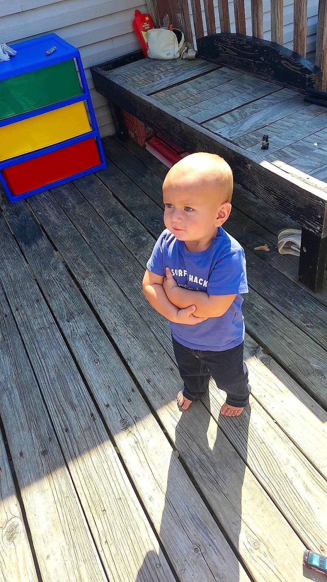 Matteo joined the competition — help win amazing prizes! toddler, child, barefoot, blue_shirt, crossed_arms, wooden_deck, sunlight, shadow, bench, toy, colorful_drawer, outdoor, playful, casual_clothing, small_toy, expression, person, daylight, standing, backyard