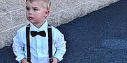 Tucker joined the competition — help win amazing prizes! child, boy, toddler, suspenders, bow_tie, white_shirt, black_pants, black_shoes, standing, outdoor, brick_wall, sidewalk, fashion, portrait, casual, young_child, looking_away, serious, cute, small