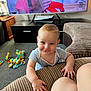 baby, blue_onesie, carpet, child, couch, cute, face, furniture, hand, happy, home, indoors, infant, leg, living_room, person, playtime, smiling, television, toy