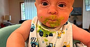Charles joined the competition — help win amazing prizes! baby, child, high_chair, bib, green_food, messy, face, hand, indoor, curious, meal, feeding, clothing, expression, person, toddler, cute, food, smear, table