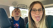Denver joined the competition — help win amazing prizes! child, adult, car_interior, glasses, tongue_out, playful, blue_shirt, black_jacket, long_hair, daylight, window, seat, headrest, person, face, silly_expression, portrait, casual_clothing, vehicle, fun