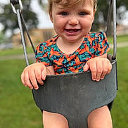 Winter is registered to the contest to win money with this photo: toddler, child, swing, playground, outdoor, grass, smiling, happy, hands, legs, clothing, short_sleeves, toy, seat, park, nature, daylight, person, face, expression