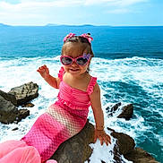 Ariana joined the competition — help win amazing prizes! child, girl, mermaid_costume, pink, sunglasses, hair_bows, rock, ocean, waves, sky, smiling, happy, outdoor, sunny, water, sea, coast, fashion, portrait, cute