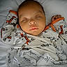 baby, bed, blanket, child, closed_eyes, clothing, comfort, cozy, cute, face, giraffe_pattern, indoors, infant, newborn, pajamas, peaceful, portrait, resting, sleeping, soft_lighting