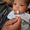 adult_hand, baby, care, child, closeup, clothing, cotton_swab, curious, eyes, face, gentle, hand, indoor, infant, mickey_mouse, person, portrait, sitting, skin, soft_lighting