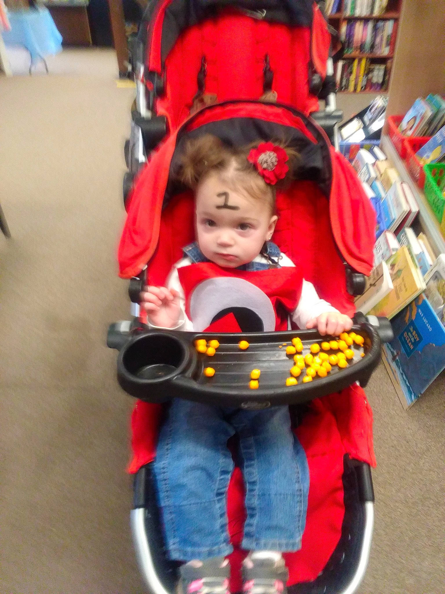 Delilah is registered to the contest to win money with this photo: baby, baby_carriage, baby_products, baby_toddler_clothing, baby_toys, bookcase, child, fun, leisure, person, play, recreation, riding_toy, shelf, sitting, tire, toddler, toy, toy_vehicle, vehicle