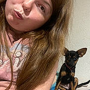Smoky is registered to the contest to win money with this photo: woman, selfie, dog, small_dog, black_dog, tan_dog, long_hair, pouty_face, bed, blanket, indoor, casual_clothing, collar, pet, cute, animal, sitting, wall, portrait, relaxed