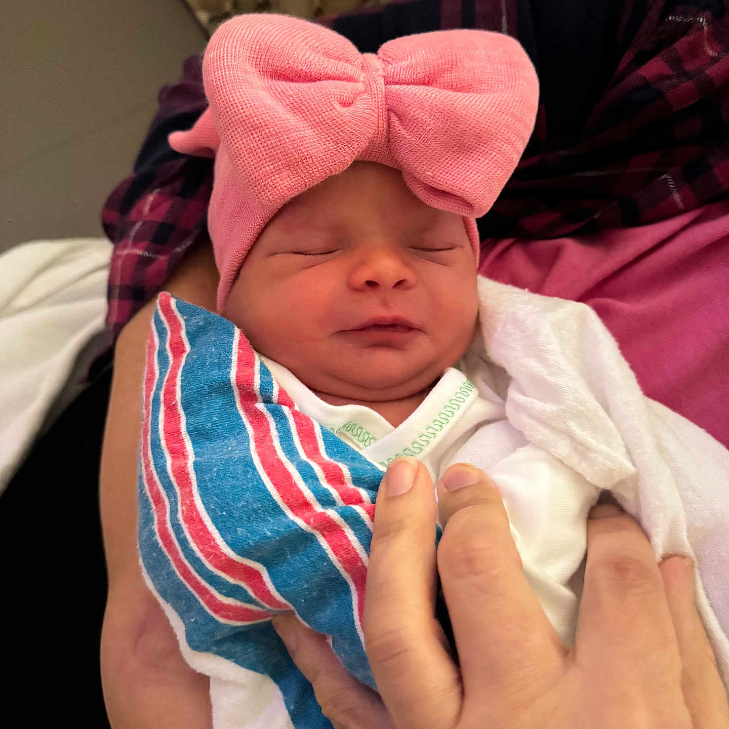 Clara joined the competition — help win amazing prizes! newborn, baby, infant, sleeping, pink_bow, hat, swaddled, blanket, hospital_blanket, portrait, face, closed_eyes, peaceful, cradled, adult_hand, parent, indoor, couch, textile, photography