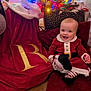Rosie joined the competition — help win amazing prizes! baby, child, christmas_tree, christmas_lights, holiday, festive_clothing, red_outfit, cushion, floor, smiling, decorations, indoor, christmas_skirt, gold_lettering, striped_leggings, happy, celebration, festive, infant, smile