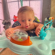 Maximus is registered to the contest to win money with this photo: activity_jumper, baby, blue_eyes, carpet, child, colorful, curly_hair, cute, expression, face, fun, furniture, hands, indoor, infant, plastic, play, room, smiling, toy