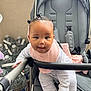 baby, child, stroller, pink_bib, hair_buns, curious_expression, indoor, water_bottles, gray_stroller, striped_clothing, playful, infant, seat, baby_clothes, toy_free, happy, cuteness, person, baby_face, baby_gear