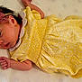 Athena is registered to the contest to win money with this photo: baby, infant, yellow_dress, pink_bow, wooden_sign, lion_illustration, month_marker, knitted_blanket, lying_down, newborn, cute, soft_lighting, portrait, child, one_month_old, baby_clothing, hand, footwear, close_up, indoor