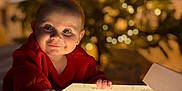 Tobie is registered to the contest to win money with this photo: baby, child, christmas_tree, cozy, curious, decorations, face, festive, gift_box, glowing, hands, happy, holiday, indoors, lights, portrait, present, red_clothing, smile, warm_lighting