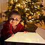 Tobie is registered to the contest to win money with this photo: baby, child, red_clothing, gift_box, christmas_tree, holiday, lights, indoors, curious, glowing, face, portrait, smile, festive, decorations, warm_lighting, hands, present, happy, cozy