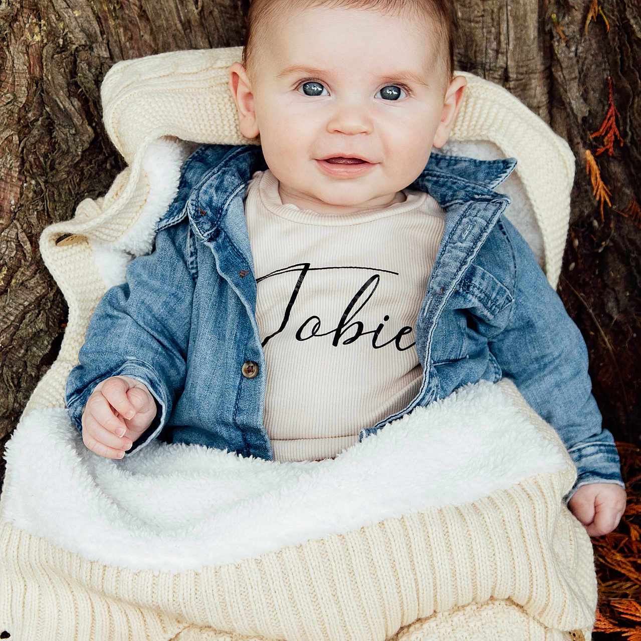 Tobie is registered to the contest to win money with this photo: baby, blanket, child, closeup, cozy, cute, denim_jacket, face, fall_leaves, happy, infant, knitwear, nature, outdoor, person, portrait, sitting, smiling, tree_trunk, warm_clothing