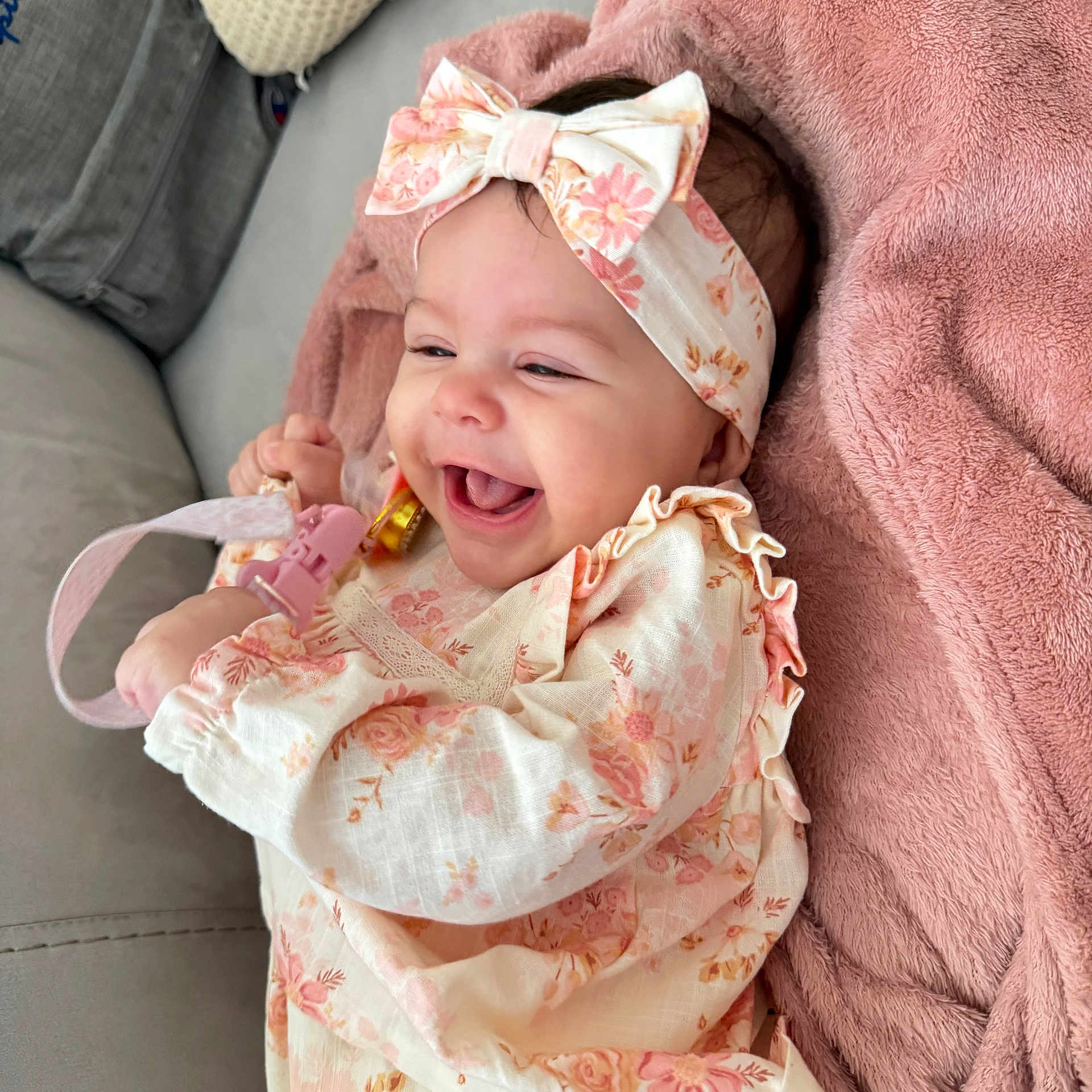 Sophia Lana is registered to the contest to win money with this photo: baby, girl, smiling, headband, bow, floral_dress, pink_blanket, pacifier_clip, happy, infant, cute, lying_down, indoors, soft_texture, child, joyful, clothing, portrait, toddler, cozy