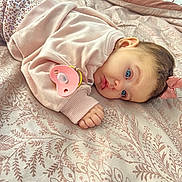 Sophia Lana is registered to the contest to win money with this photo: baby, pacifier, blue_eyes, pink_bow, bedspread, patterned_fabric, infant, sleepwear, hand, face, lying_down, soft_light, cute, child, portrait, indoors, resting, closeup, person, small_hands