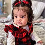 bed, black_checkered, blanket, child, clothing, cozy, curly_hair, cute, expression, face, indoor, person, portrait, red_bows, red_vest, sitting, soft_lighting, toddler, white_shirt, young_child