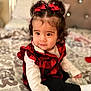 Abigail is registered to the contest to win money with this photo: baby, bed, black_pants, blanket, checkered_vest, child, cozy, curly_hair, cute, face, indoors, person, portrait, red_bows, sitting, smiling, soft_lighting, toddler, white_shirt, young_child
