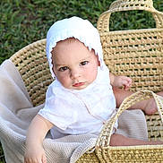 Shmaya is registered to the contest to win money with this photo: baby, child, basket, white_clothing, bonnet, blanket, grass, outdoor, toy, wooden_toy, cute, infant, sitting, portrait, soft_light, natural_light, woven_basket, serious_expression, close_up, person