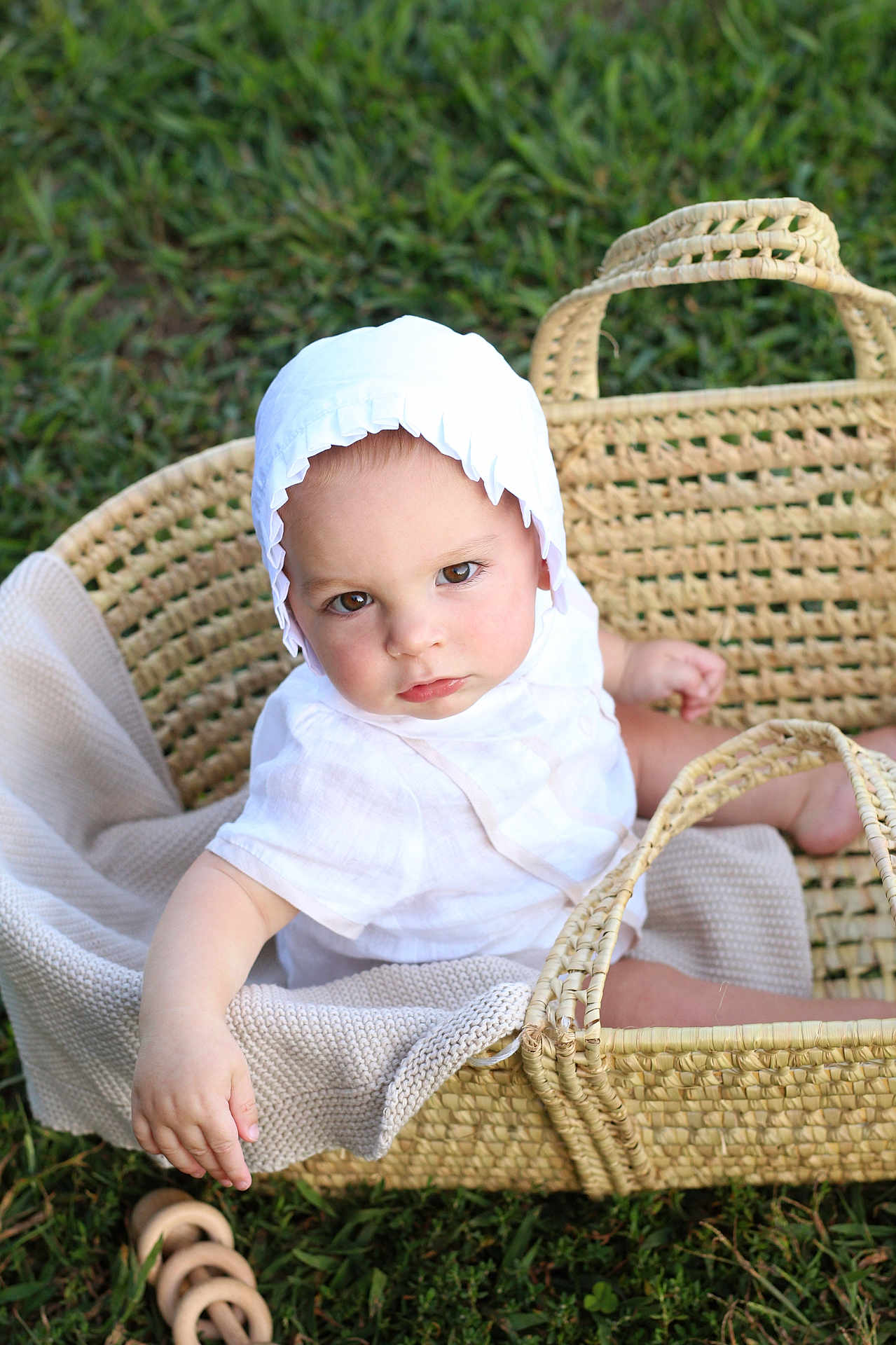 Shmaya is registered to the contest to win money with this photo: baby, child, basket, white_clothing, bonnet, blanket, grass, outdoor, toy, wooden_toy, cute, infant, sitting, portrait, soft_light, natural_light, woven_basket, serious_expression, close_up, person