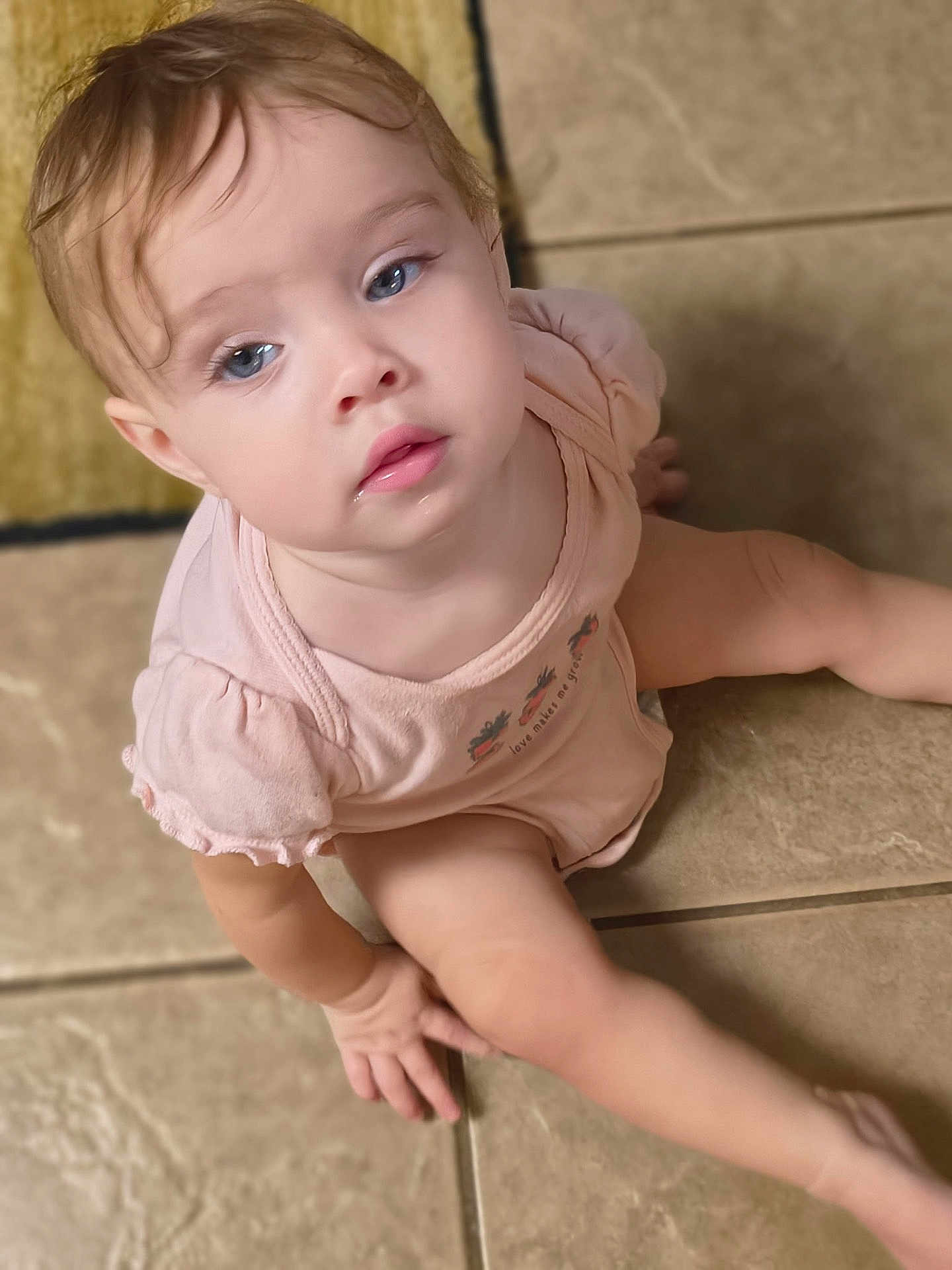Payton is registered to the contest to win money with this photo: toddler, child, baby, sitting, floor, tile, blue_eyes, pink_clothing, curly_hair, indoor, portrait, cute, soft_lighting, hand, face, expression, casual, young, person, skin