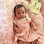 Milani is registered to the contest to win money with this photo: baby, infant, pink_dress, blanket, hearts, wooden_sign, butterflies, lying_down, cute, smiling, face, hands, feet, soft_texture, pattern, child, person, portrait, indoors, adorable