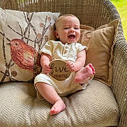 Leland is registered to the contest to win money with this photo: baby, infant, smiling, wicker_chair, cushion, plaque, wooden_sign, five_months, happy, cute, indoors, clothing, sitting, child, portrait, person, relaxing, decor, couch, feet