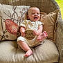 baby, infant, smiling, wicker_chair, cushion, plaque, wooden_sign, five_months, happy, cute, indoors, clothing, sitting, child, portrait, person, relaxing, decor, couch, feet