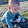 Leland is registered to the contest to win money with this photo: baby, child, plush_toy, rocky_beach, pebbles, seaweed, blue_pajamas, outdoor, sunlight, curious, exploring, sitting, nature, closeup, infant, person, daylight, soft_toy, cute, portrait