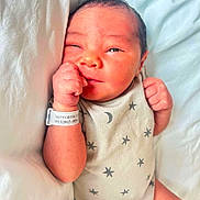 Zayden is registered to the contest to win money with this photo: newborn, baby, infant, onesie, stars, moon, hospital_bracelet, bed, blanket, sleepwear, cute, skin, hand, face, expression, portrait, resting, indoors, person, young_child