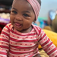 Jianna is registered to the contest to win money with this photo: baby, infant, smiling, headband, bow, striped_clothing, hearts, tongue_out, cute, portrait, indoors, happy, child, young, person, face, skin, sitting, apparel, fashion