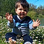 toddler, child, smiling, flowers, daisies, grass, outdoor, nature, sunny, blue_sky, lake, trees, barefoot, sitting, casual_clothing, greenery, spring, happy, playful, portrait
