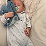 baby, sleeping, pacifier, plush_toy, onesie, couch, pillow, blanket, infant, child, resting, comfort, soft_toy, indoor, peaceful, cozy, clothing, hand, face, relaxation