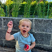 Isaac a rejoint le concours — aidez-le/la à gagner de superbes lots ! toddler, child, outdoor, greenery, stone_wall, wooden_surface, seed, container, happy, smiling, short_hair, blue_onesie, necklace, sunlight, nature, baby, person, playful, summer, garden